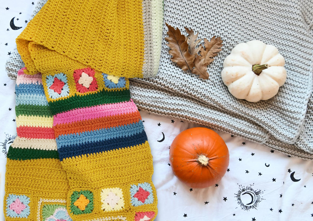 Golden granny square crochet scarf displayed with knitted blankets and pumpkins in a cozy setting
