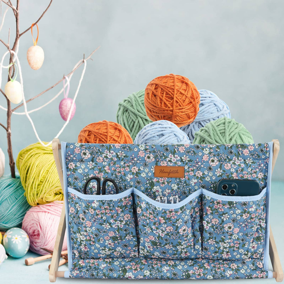Woolique blue floral-patterned craft organizer, set against an Easter-themed backdrop with decorated eggs and yarn
