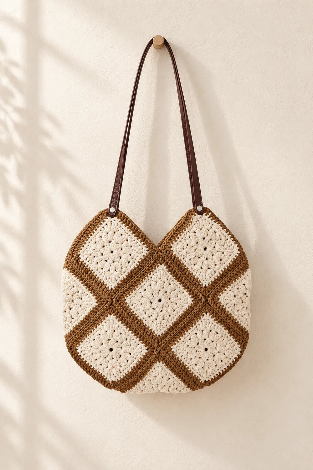 La borsa completa a quadrati granny color crema e moka, inclusi i lunghi manici marroni, davanti a una parete avorio