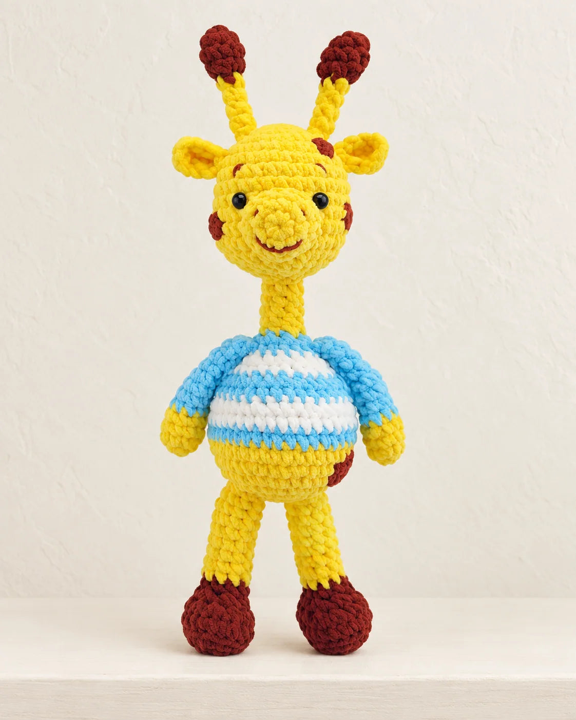 Plush crochet giraffe design with yellow, blue, brown and white yarn details